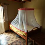 Rede mosquiteira colocada sobre uma cama em habitação familiar simples, exemplificando a prevenção da malária em comunidade.