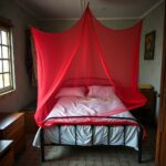 Rede mosquiteira estendida sobre uma cama num quarto arrumado em habitação familiar moçambicana.