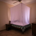 Quarto familiar humilde e bem cuidado com rede mosquiteira branca instalada sobre a cama.