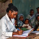 Profissional de saúde comunitária preenchendo registos de acompanhamento materno-infantil em comunidade rural moçambicana.