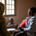 Profissional de saúde segura cartão de pré-natal durante consulta de acompanhamento materno-infantil em centro de saúde comunitário.